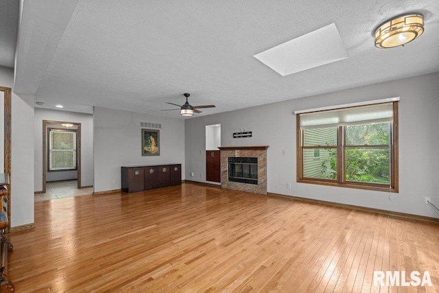 unfurnished living room featuring baseboards, a high end fireplace, a ceiling fan, light wood-style flooring, and a skylight