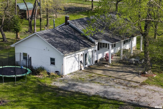 view of home's exterior featuring roof with shingles, a trampoline, an attached garage, a chimney, and a lawn