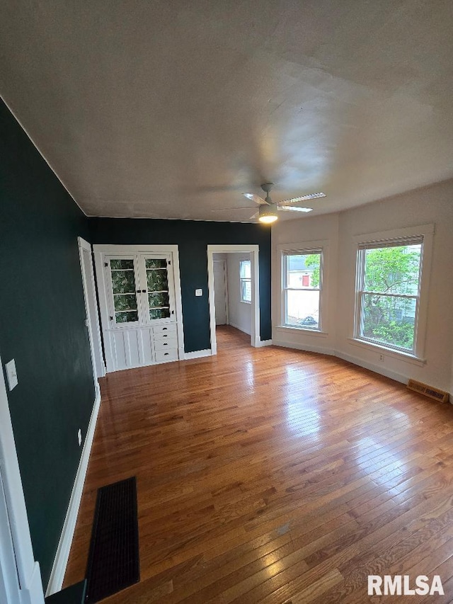 unfurnished living room with ceiling fan, baseboards, visible vents, and wood finished floors