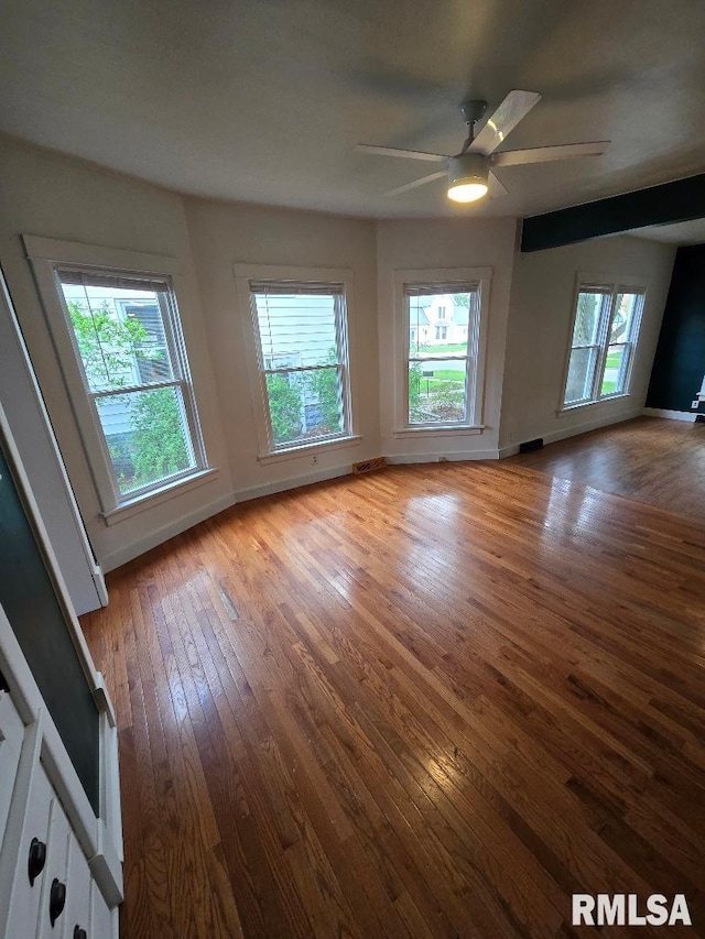 unfurnished room with wood-type flooring, a ceiling fan, and baseboards