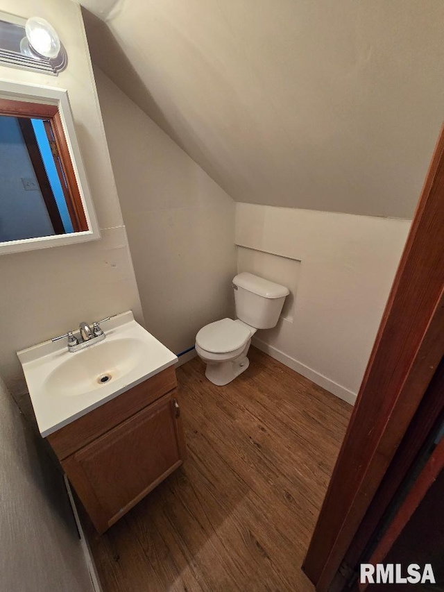 half bathroom featuring wood finished floors, lofted ceiling, toilet, and vanity