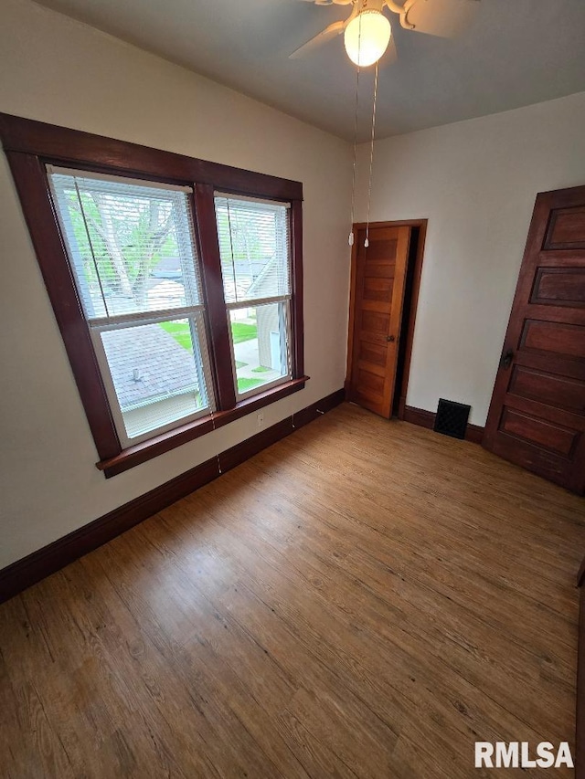 spare room with baseboards, a ceiling fan, wood finished floors, and a wealth of natural light