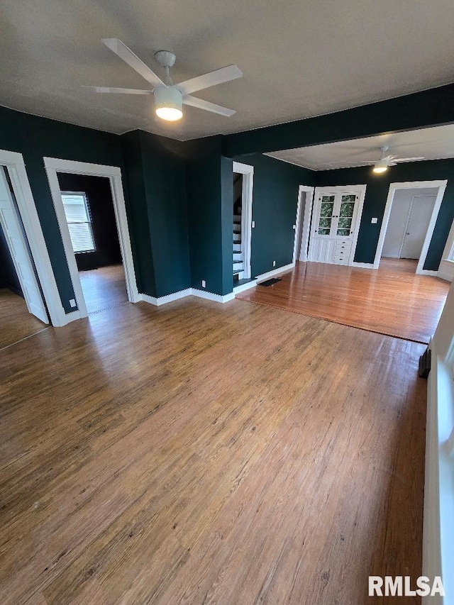 unfurnished living room with baseboards, stairs, ceiling fan, and wood finished floors