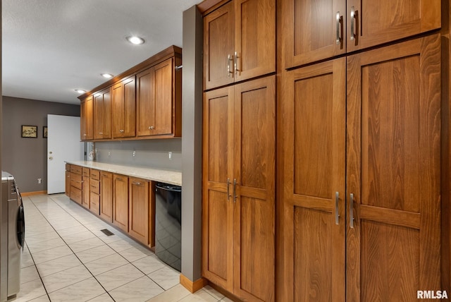 kitchen with brown cabinetry, washer / dryer, baseboards, black dishwasher, and light tile patterned floors