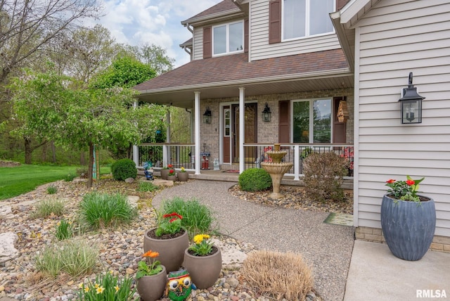 doorway to property featuring covered porch and a shingled roof