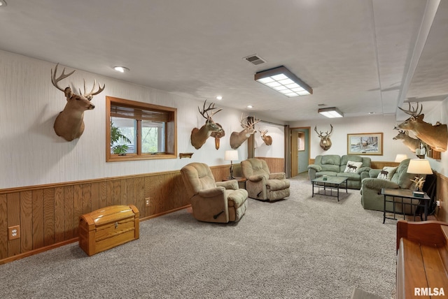 carpeted living room with wood walls, visible vents, and wainscoting
