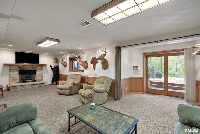 living room featuring visible vents, a fireplace, wooden walls, a wainscoted wall, and carpet