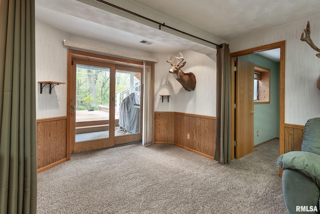 unfurnished room with carpet, wainscoting, wood walls, and visible vents