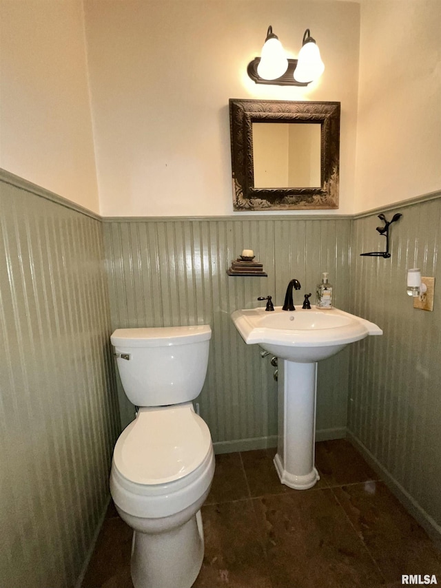 half bathroom with toilet, tile patterned floors, and wainscoting