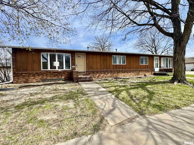 ranch-style home with board and batten siding, a front lawn, and brick siding