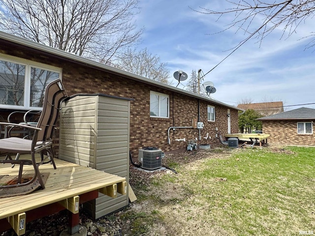 rear view of house with central air condition unit, brick siding, a yard, and a wooden deck