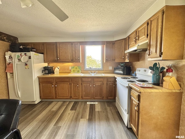 kitchen featuring white appliances, a textured ceiling, under cabinet range hood, a sink, and light wood finished floors