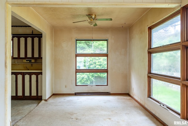 unfurnished room featuring ceiling fan, carpet, a healthy amount of sunlight, and a baseboard heating unit