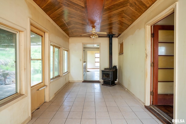 interior space with a wood stove, light tile patterned flooring, crown molding, a ceiling fan, and wood ceiling