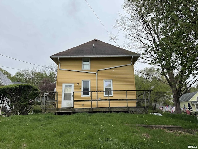 rear view of property featuring a yard, a wooden deck, and roof with shingles