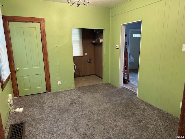 carpeted spare room with an inviting chandelier, wooden walls, and visible vents