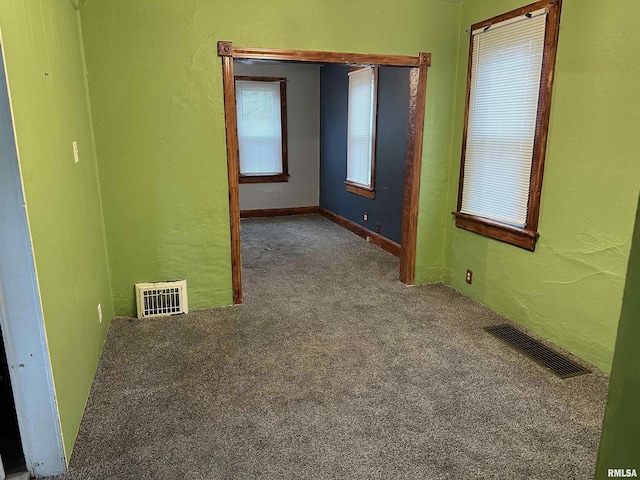 empty room with carpet flooring, visible vents, and a textured wall