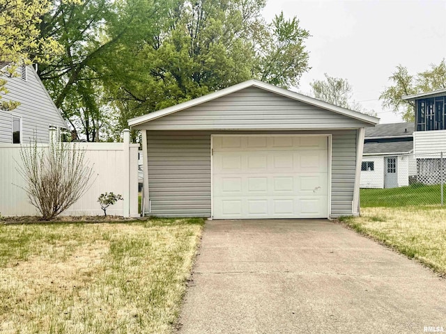 detached garage featuring concrete driveway and fence