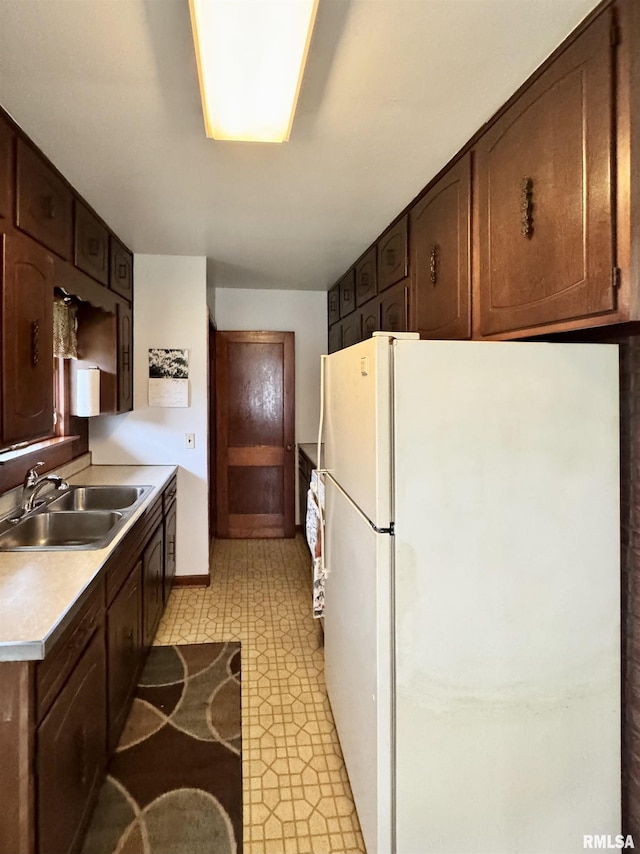 kitchen featuring a sink, freestanding refrigerator, light floors, light countertops, and baseboards