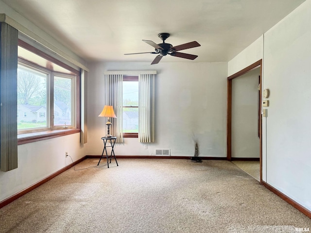 carpeted empty room with baseboards, ceiling fan, and visible vents