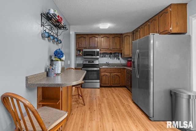 2303 Pinehurst St, Bettendorf, IA 52722 - kitchen with stainless steel appliances, a sink, brown cabinetry, light wood finished floors, and open shelves