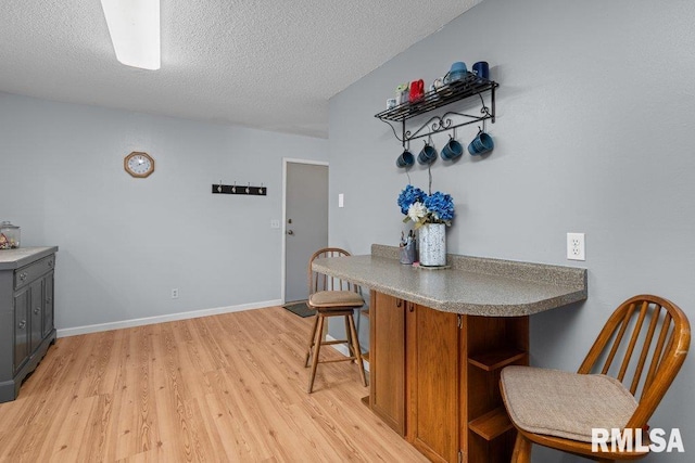 2303 Pinehurst St, Bettendorf, IA 52722 - kitchen with open shelves, light wood-style floors, a peninsula, a textured ceiling, and a breakfast bar area