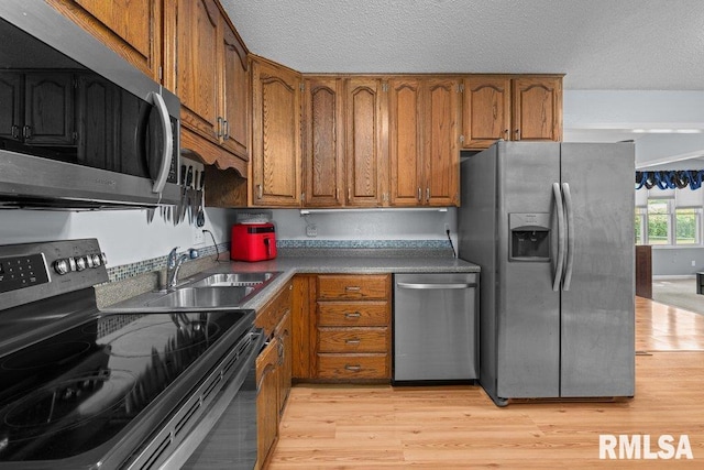 2303 Pinehurst St, Bettendorf, IA 52722 - kitchen with stainless steel appliances, brown cabinetry, light wood-type flooring, a sink, and a textured ceiling