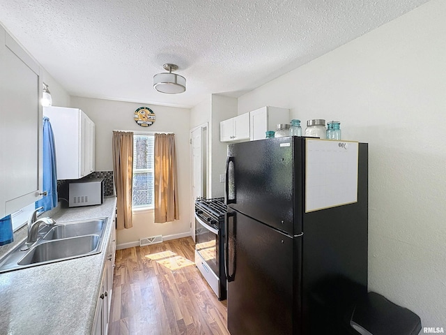 kitchen with a sink, freestanding refrigerator, light wood-type flooring, visible vents, and stainless steel range with gas cooktop