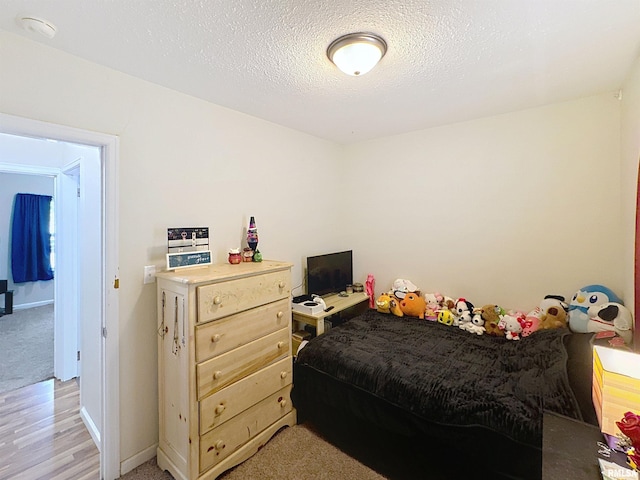 bedroom featuring light wood finished floors, a textured ceiling, and baseboards
