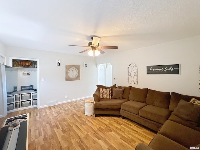 living room featuring light wood finished floors, a ceiling fan, visible vents, baseboards, and arched walkways