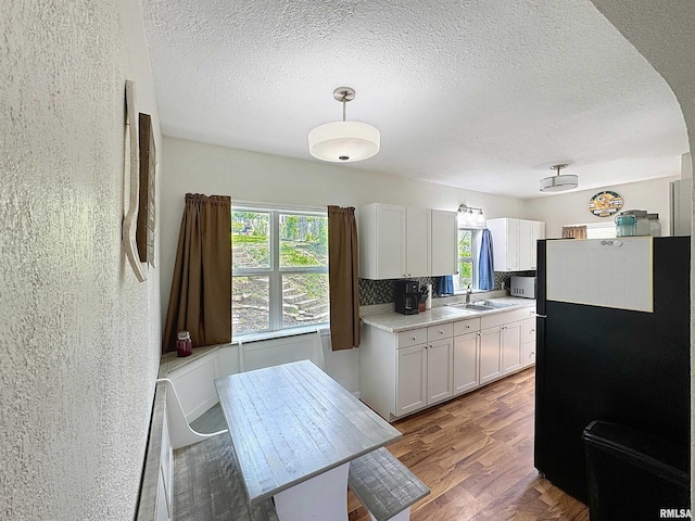 kitchen with wood finished floors, a sink, freestanding refrigerator, white cabinetry, and light countertops