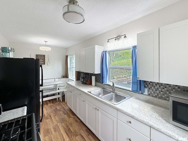 kitchen featuring a sink, freestanding refrigerator, a textured ceiling, stainless steel microwave, and decorative backsplash
