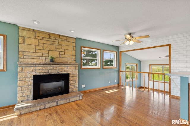 unfurnished living room featuring ceiling fan, wood finished floors, baseboards, and a stone fireplace