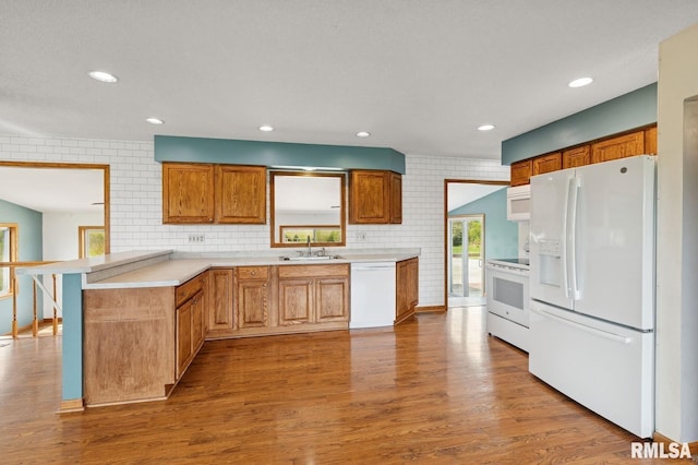 kitchen with a sink, a peninsula, white appliances, light wood finished floors, and light countertops