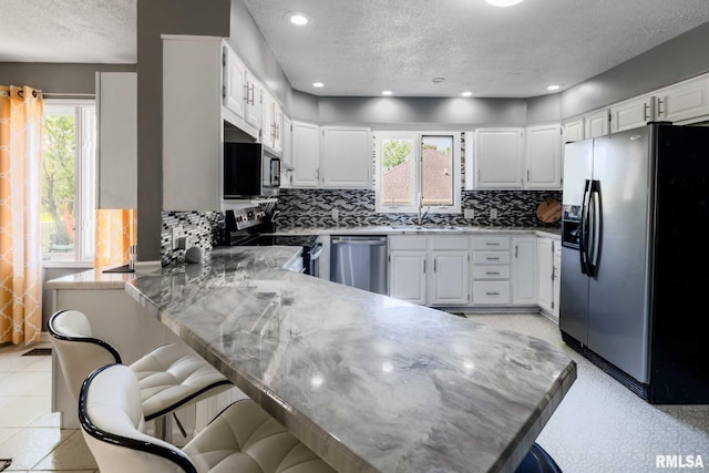 kitchen featuring a textured ceiling, a kitchen breakfast bar, a healthy amount of sunlight, and appliances with stainless steel finishes