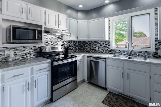 kitchen with a sink, stainless steel appliances, under cabinet range hood, light countertops, and decorative backsplash