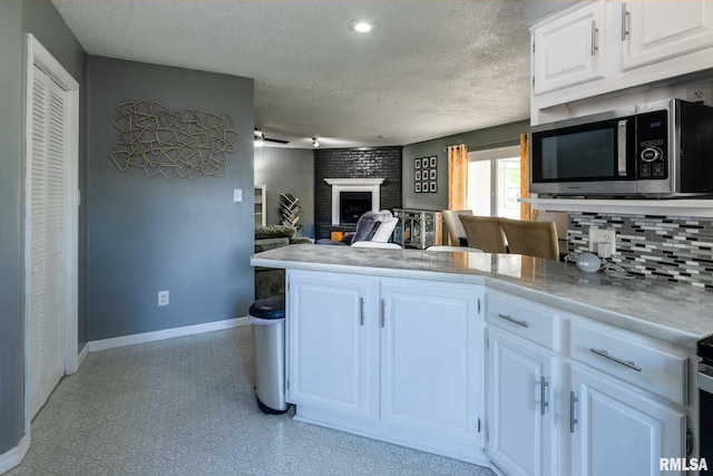 kitchen with a textured ceiling, baseboards, stainless steel microwave, white cabinetry, and a peninsula