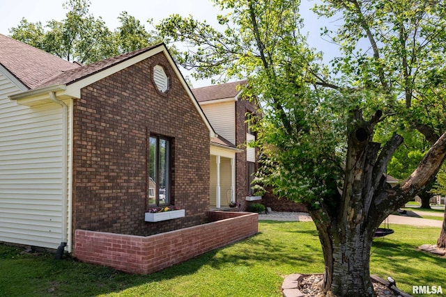view of side of home featuring a yard, roof with shingles, and brick siding