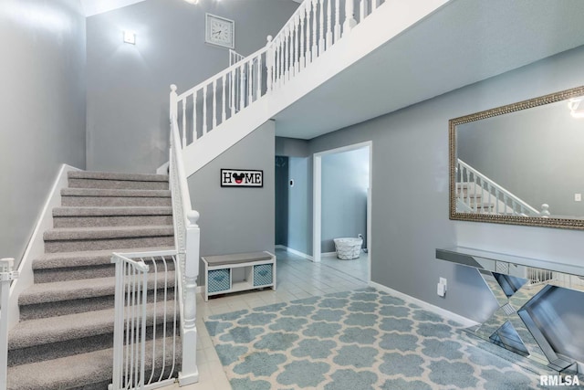 staircase featuring tile patterned floors, baseboards, and a high ceiling