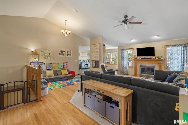 living area with a fireplace, lofted ceiling, ceiling fan with notable chandelier, and light wood-style flooring