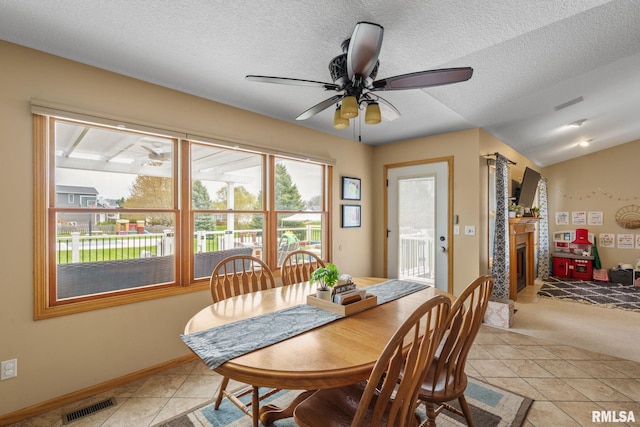 dining space featuring light tile patterned floors, a textured ceiling, visible vents, ceiling fan, and a glass covered fireplace