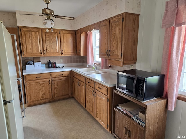 kitchen featuring freestanding refrigerator, wallpapered walls, a sink, stainless steel microwave, and light countertops