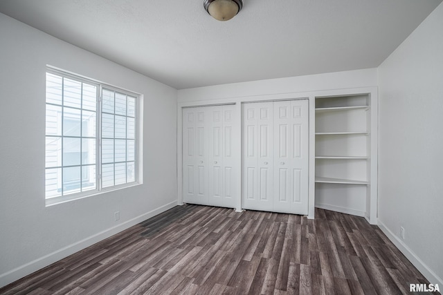 unfurnished bedroom with two closets, dark wood-style flooring, and baseboards