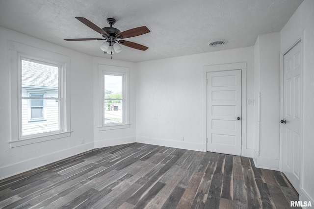 empty room with baseboards, a textured ceiling, visible vents, and dark wood-style floors