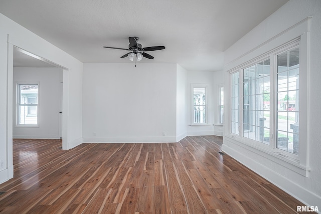 empty room featuring a wealth of natural light, dark wood finished floors, and baseboards