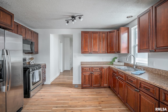 kitchen with a sink, stainless steel appliances, a textured ceiling, light wood-type flooring, and baseboards