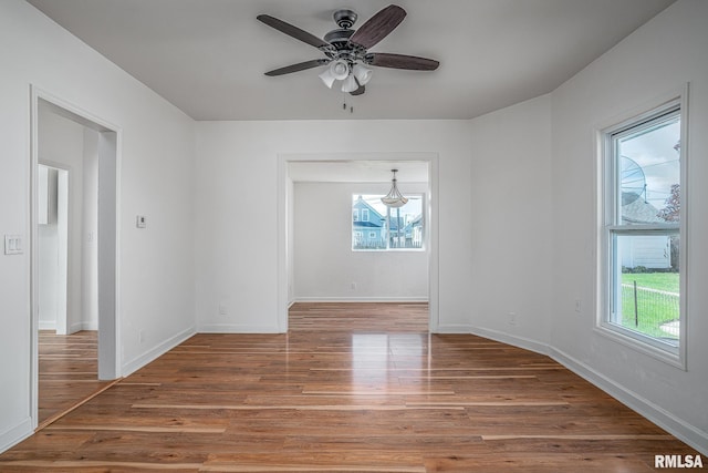 spare room with plenty of natural light, ceiling fan with notable chandelier, and light wood-type flooring