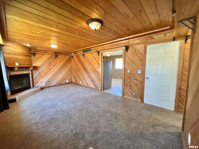 unfurnished living room with wooden walls, carpet, wood ceiling, and a tiled fireplace