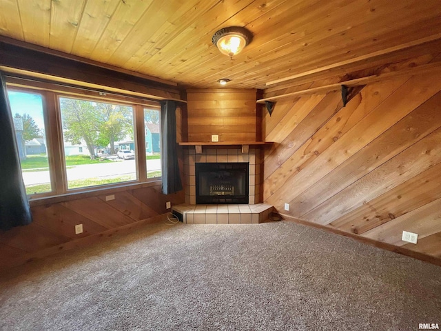 unfurnished living room featuring wooden ceiling, wood walls, carpet floors, and a tiled fireplace