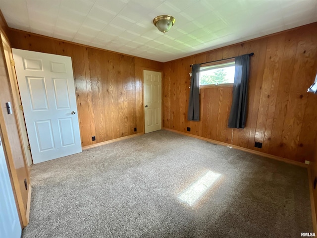 empty room featuring wood walls, carpet flooring, and baseboards